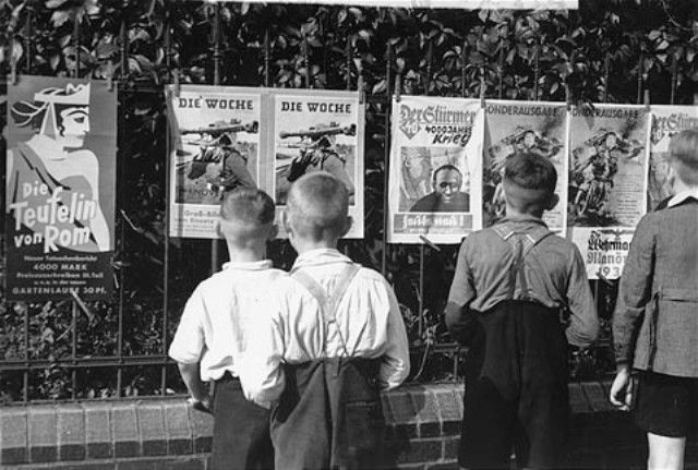 German boys view propaganda posters that are posted on a fence in Berlin